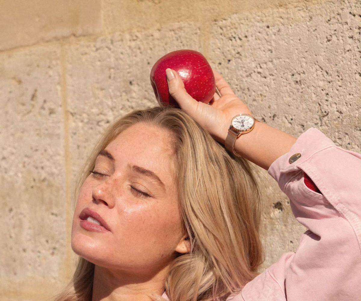 A woman wearing a pink jacket, with an apple on her head and a rose-gold Charlie Paris watch on her wrist