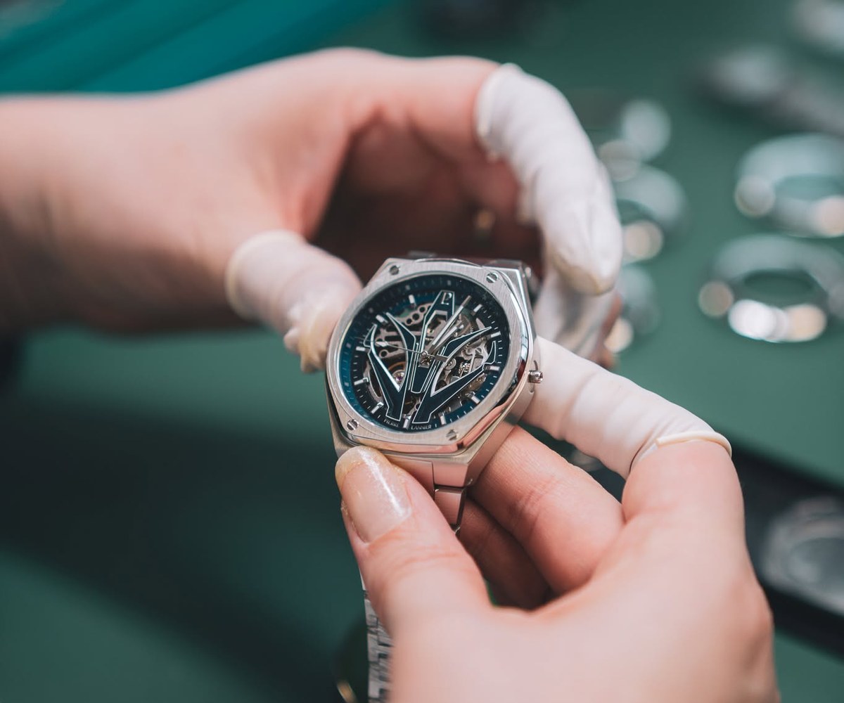 Mains gantees tenant une montre en acier sur un etabli d'horloger