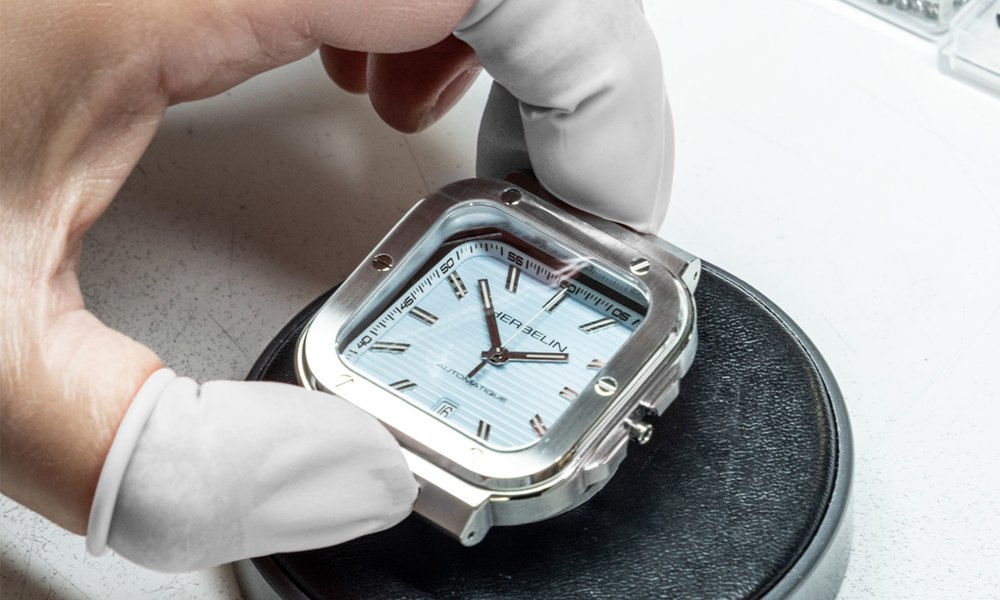 Horloger ganté ouvrant le boitier d'une montre sur un outil d'atelier pour verifier les joints d'etancheite