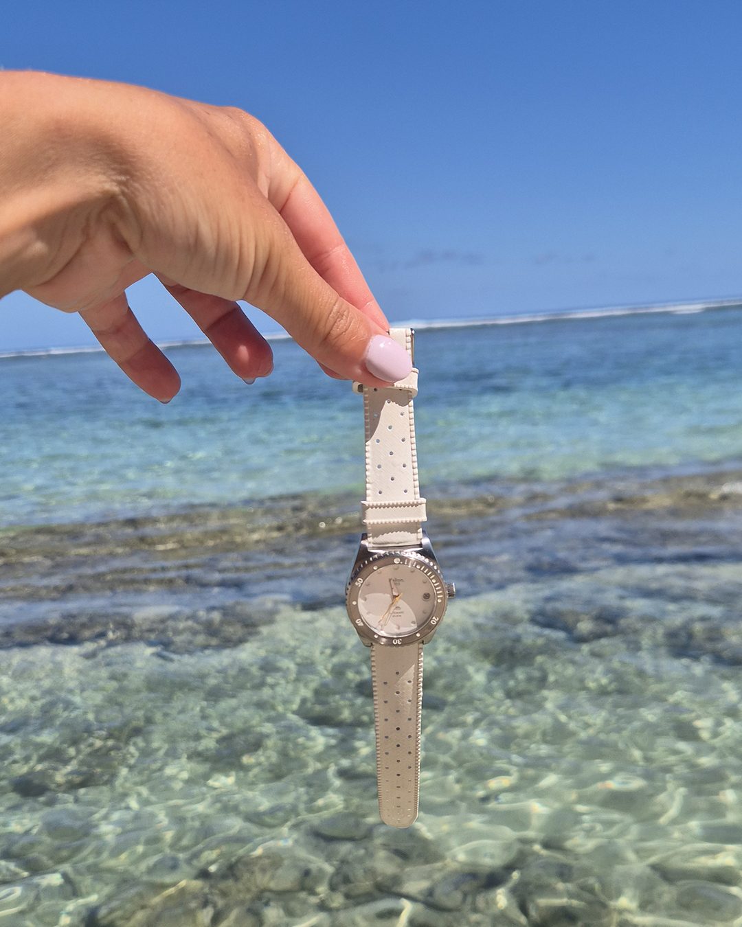 Montre Kelton blanche tenue au-dessus d'un lagon turquoise