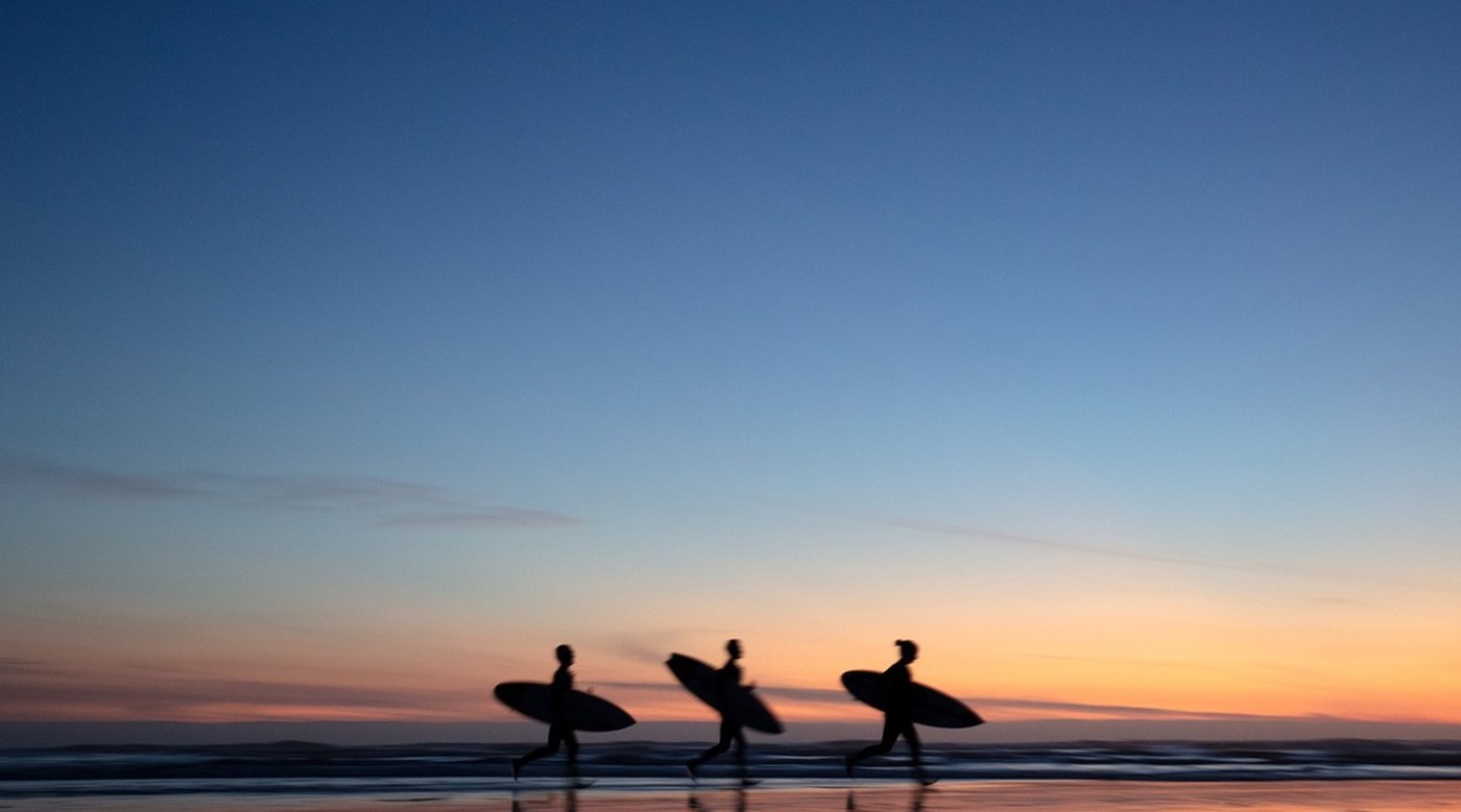 Surfeurs marchant sur la plage au coucher du soleil, planches sous le bras