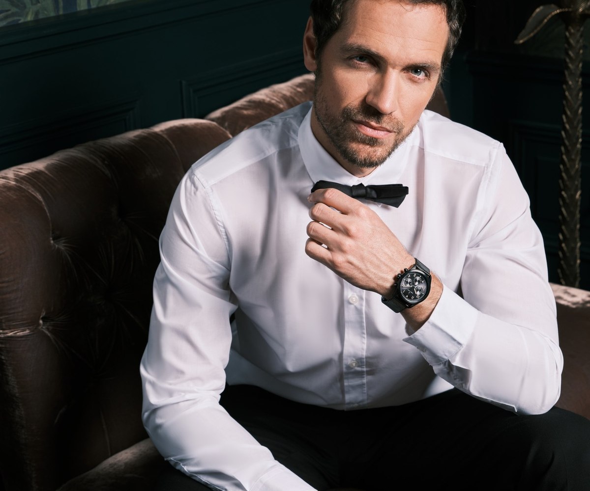 Homme en chemise blanche portant une montre squelette, fauteuil en cuir