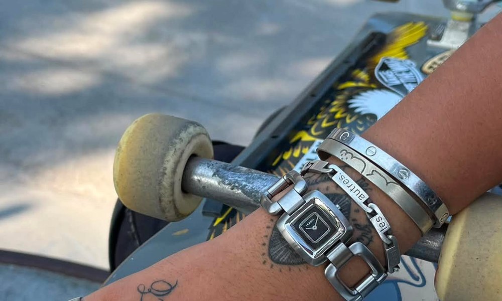 Poignet d'adolescent avec montre et bracelets pose sur un skateboard