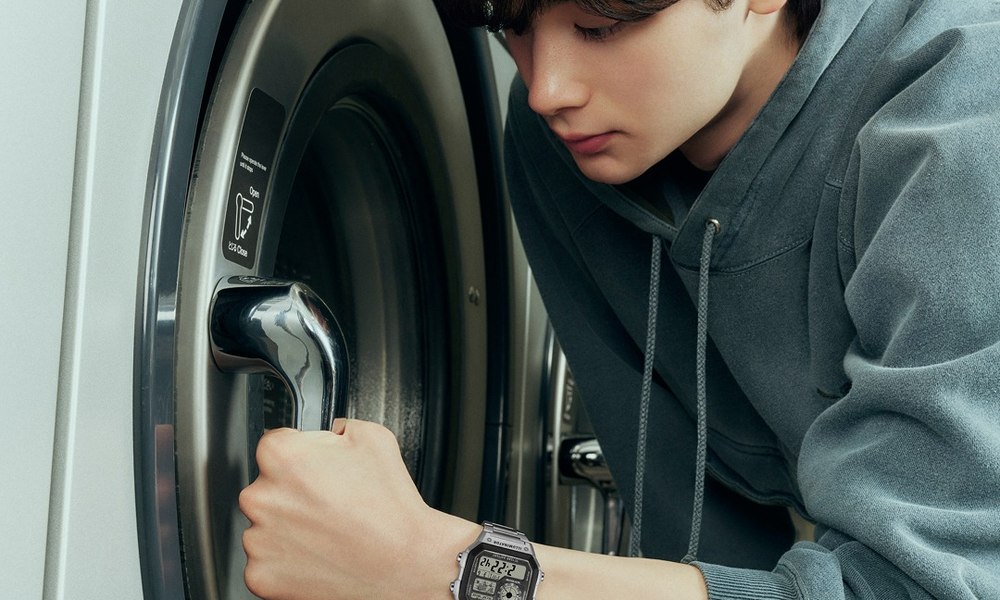 Jeune homme en sweat devant une laverie automatique, montre digitale au poignet