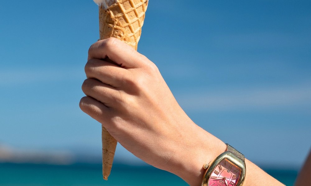 Main tenant une glace devant la mer, montre etanche coloree au poignet