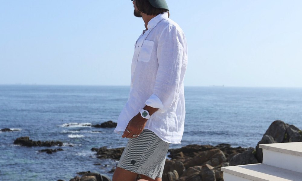 Homme en chemise de lin blanche et short au bord de la mer, montre etanche au poignet