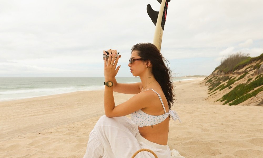 Jeune femme en maillot de bain assise sur la plage, panier en osier et montre etanche coloree