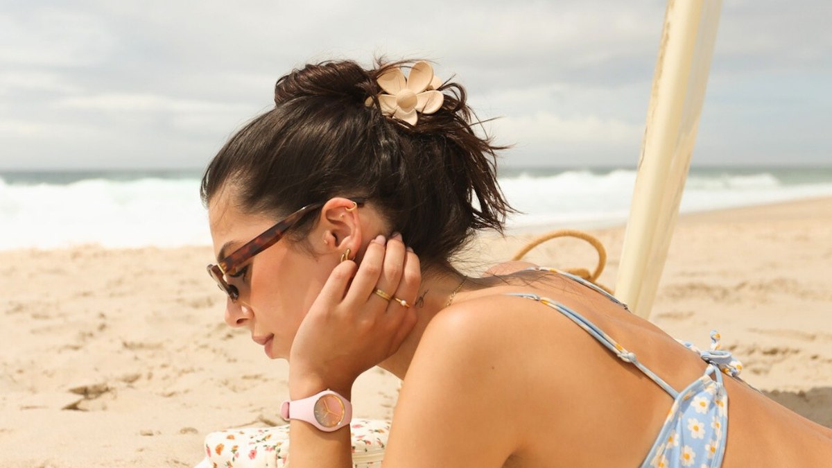 Jeune femme en maillot de bain allongee sur la plage, montre etanche rose au poignet