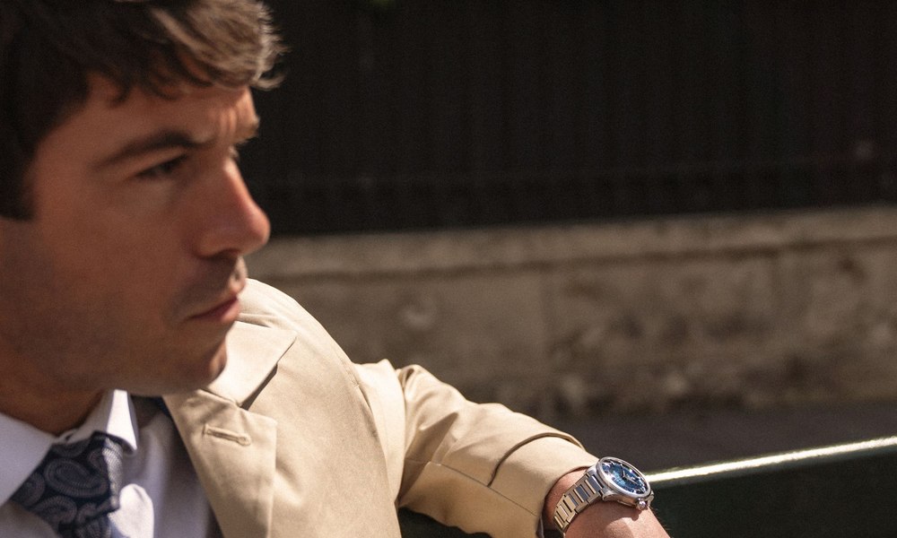 Homme en costume de lin clair et cravate, montre habillee a cadran bleu au poignet