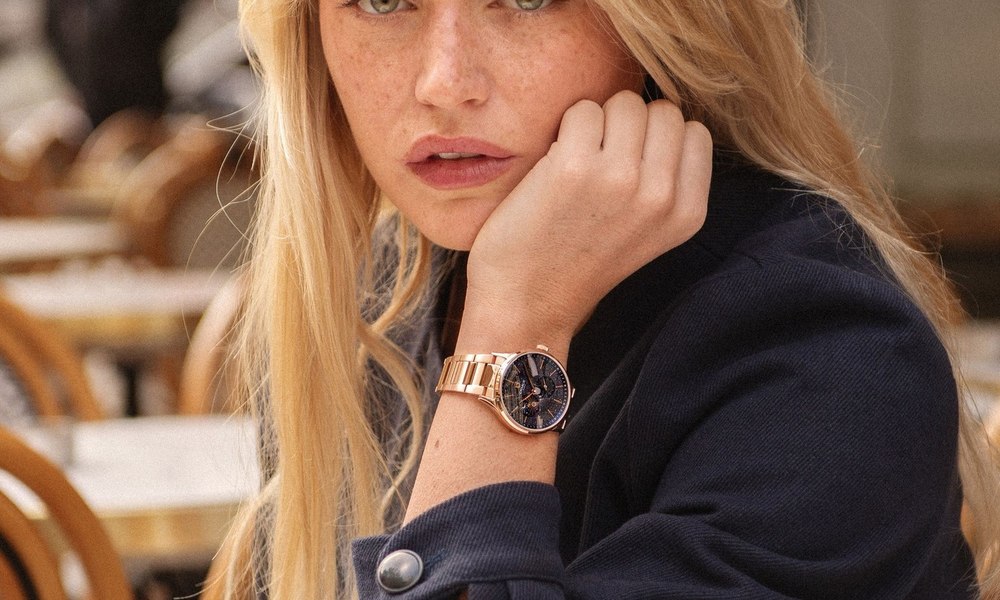 Jeune femme a la terrasse d'un cafe en ete, montre doree a bracelet maille au poignet