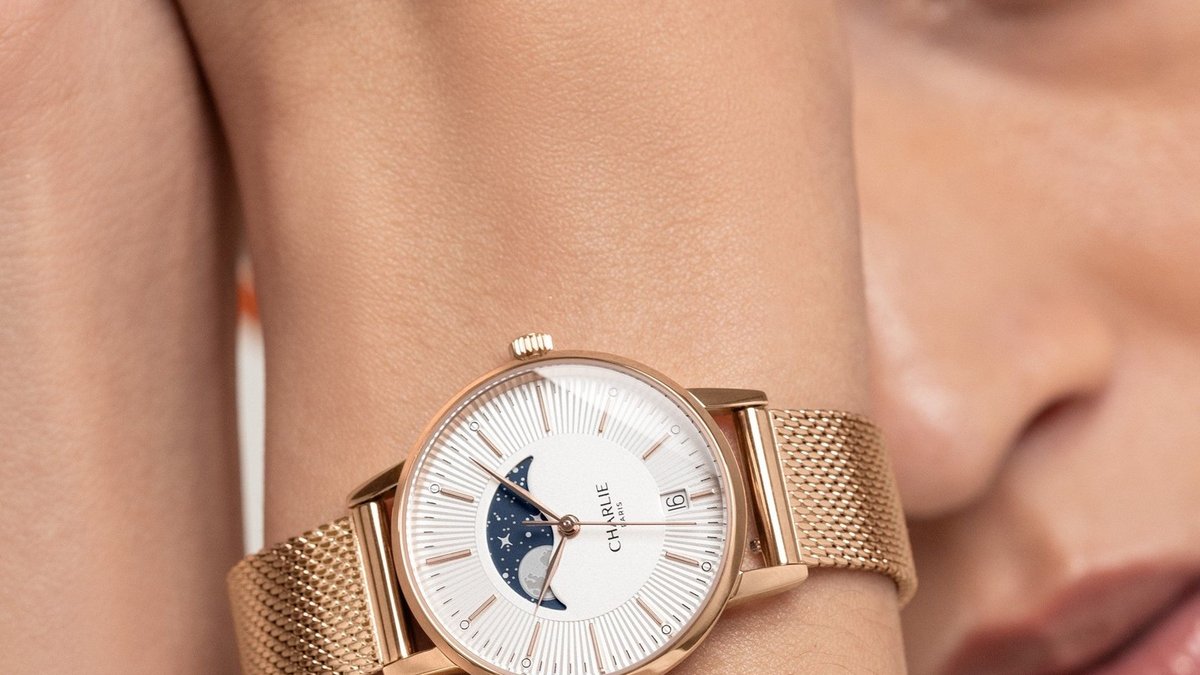 Poignet de femme portant une montre dorée Charlie Paris au soleil d'été