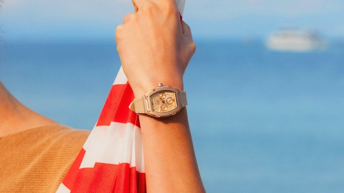 Montre Ice-Watch au poignet sous le soleil de la plage, parasol rayé rouge et blanc