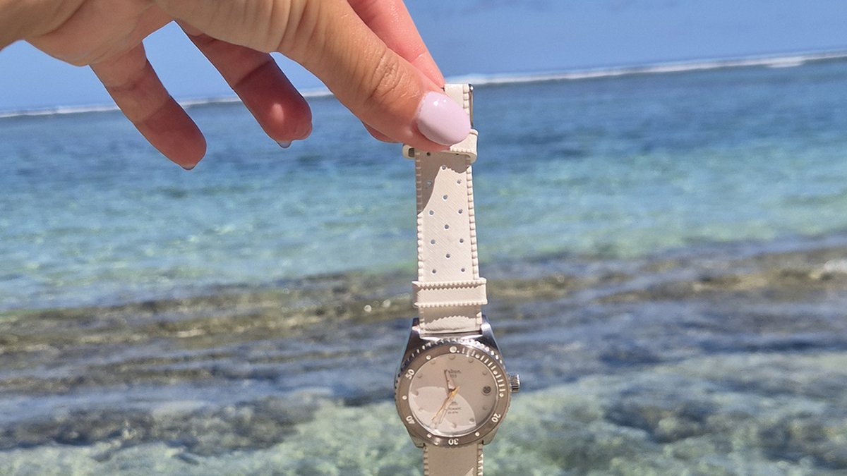 A white French watch suspended above a turquoise lagoon