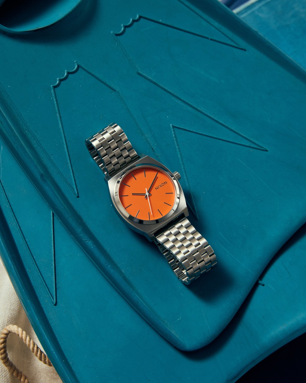 Montre Nixon Time Teller acier &agrave; cadran orange pos&eacute;e sur un bodyboard