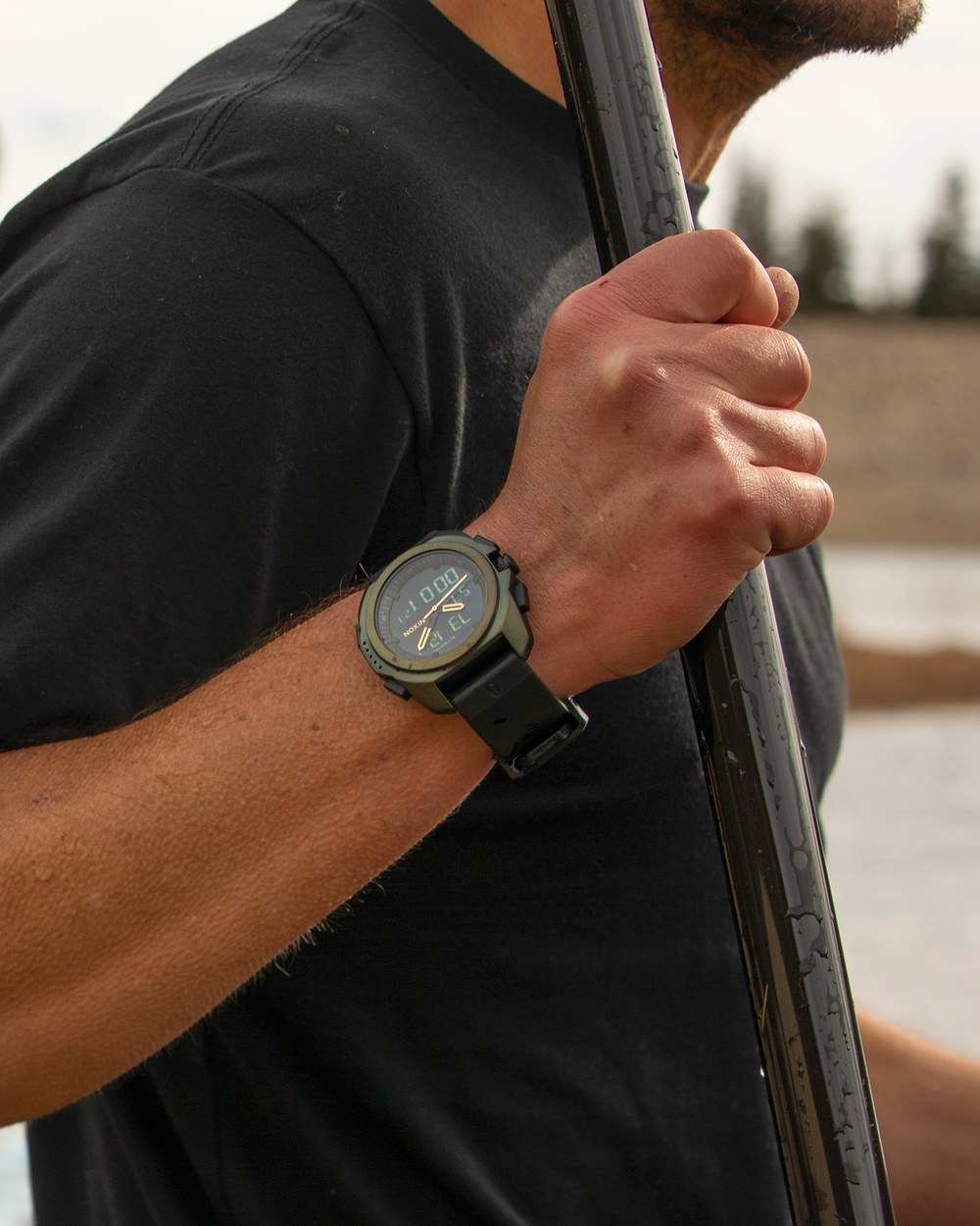 Montre Nixon au poignet d'un surfeur portant sa planche